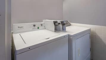 A Whirlpool front-loading washer and dryer in a laundry room with white tiled walls and a fluorescent light above the appliances.