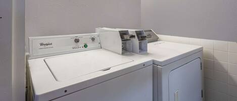 A Whirlpool front-loading washer and dryer in a laundry room with white tiled walls and a fluorescent light above the appliances.