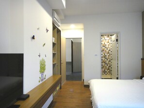 A hotel room with a bed, a wooden bench, a TV, a wardrobe, and a bathroom visible through an open door.