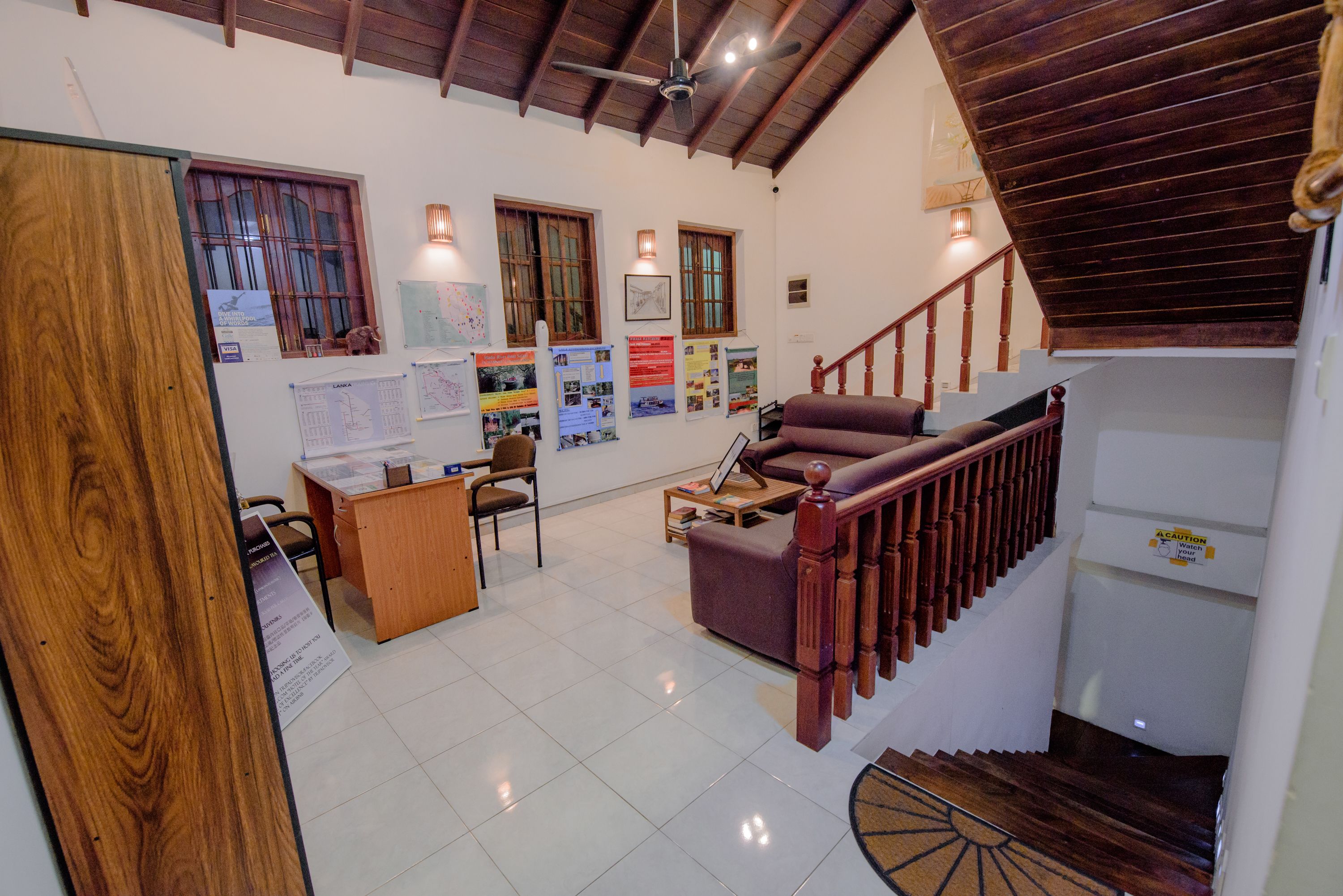 A spacious living area with a wooden staircase, a sofa, a desk, and various wall decorations.
