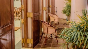 Um corredor com portas de madeira, cadeiras de vime e um vaso de plantas.