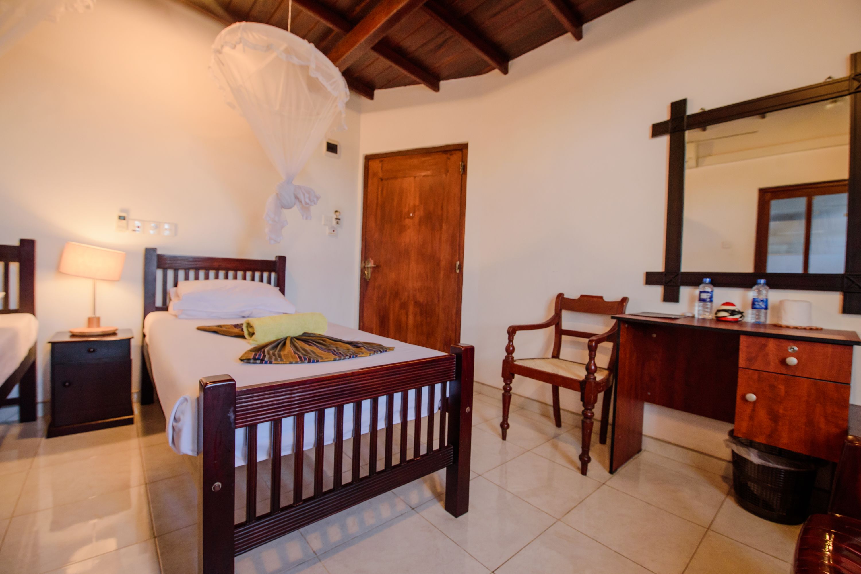 A bedroom with a wooden bed, bedside tables, a chair, a desk, and a mirror.