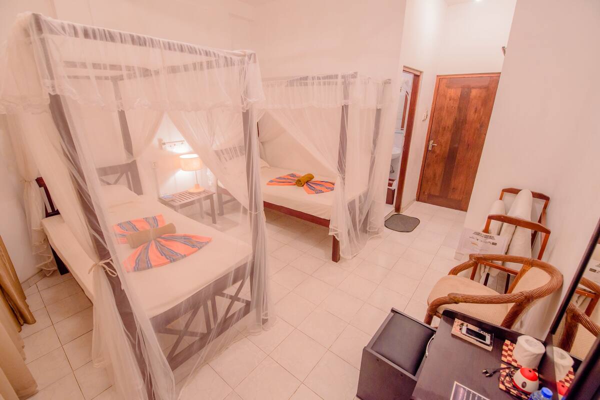 A room with two beds covered by mosquito nets, a desk with a computer, and a chair.