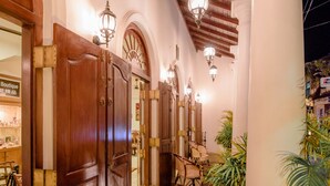 Corredor com portas de madeira, chão de pedra e um pilar branco.