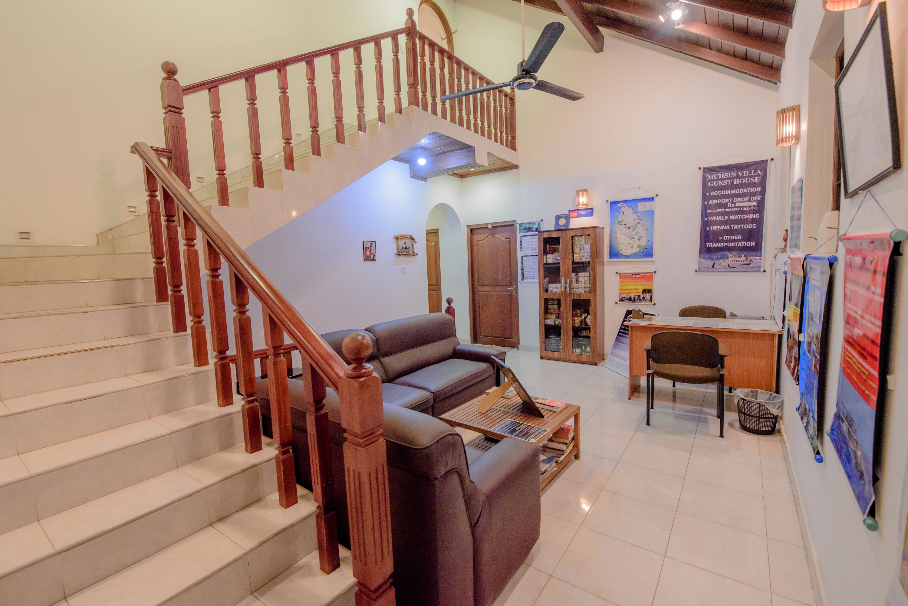 A spacious living area with a staircase, a sofa, a desk, and a ceiling fan.