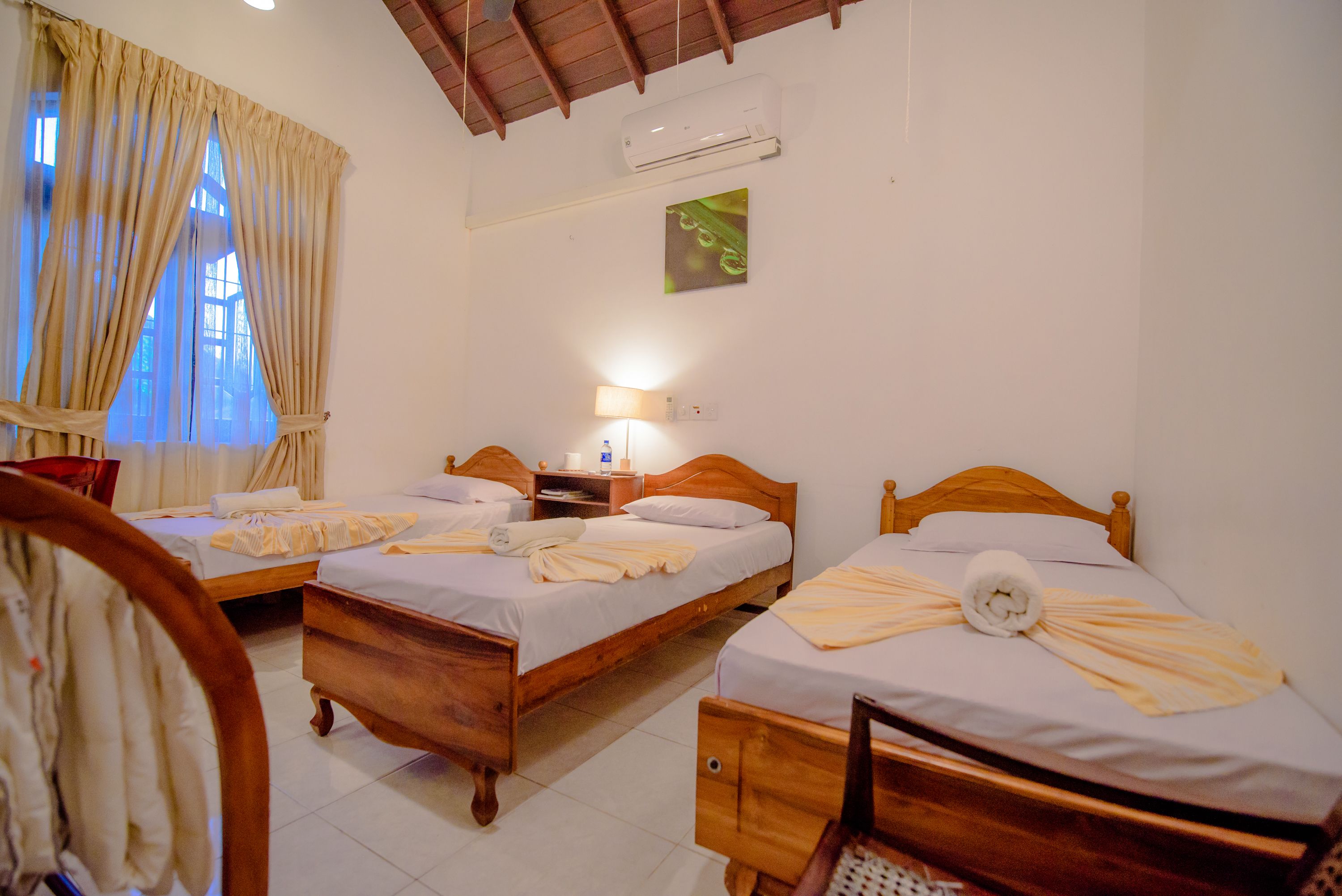 A hotel room with two wooden beds, a nightstand, a lamp, and a window with curtains.