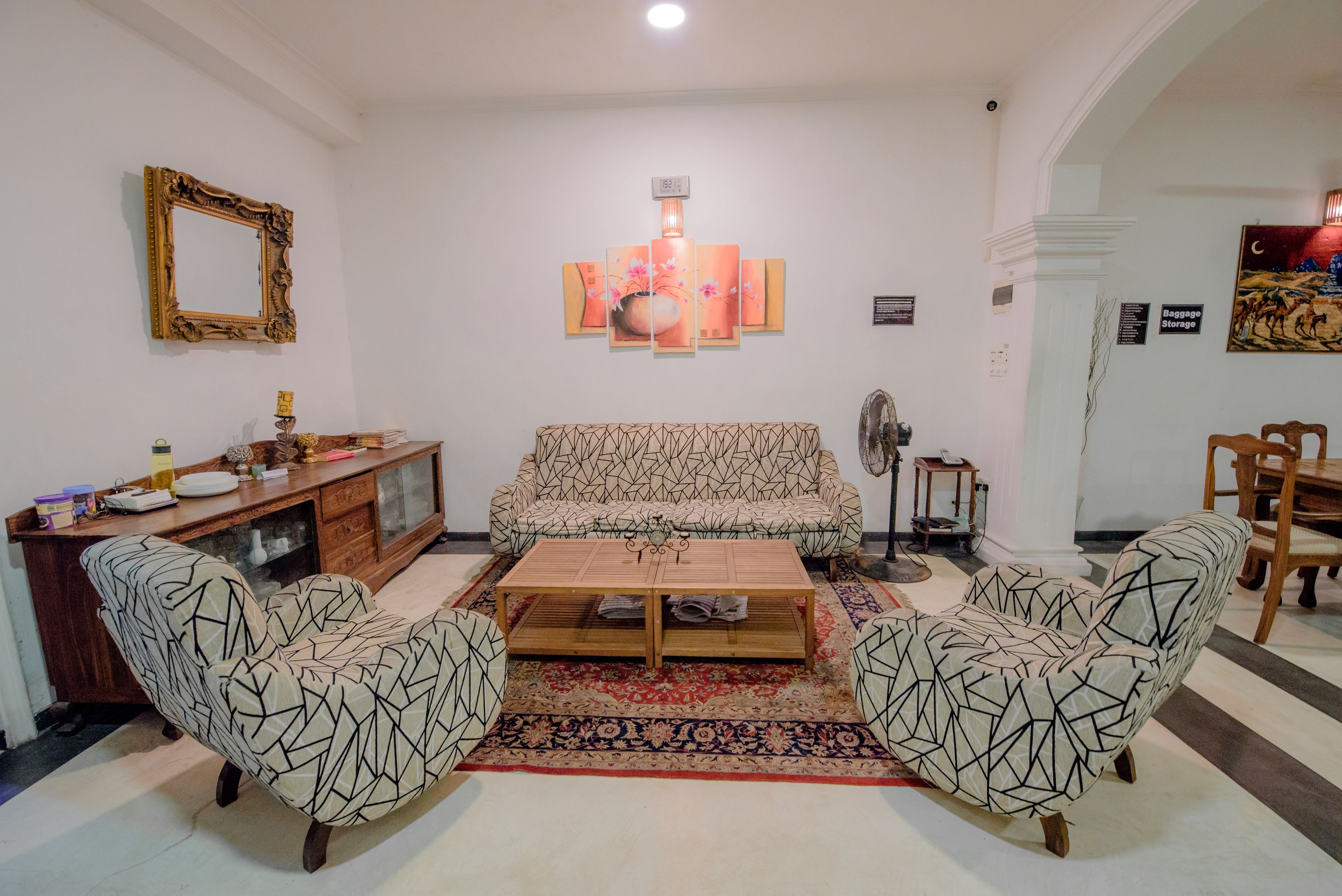 A living room with a sofa, two armchairs, a coffee table, a patterned rug, a decorative lamp, and a wall-mounted mirror.