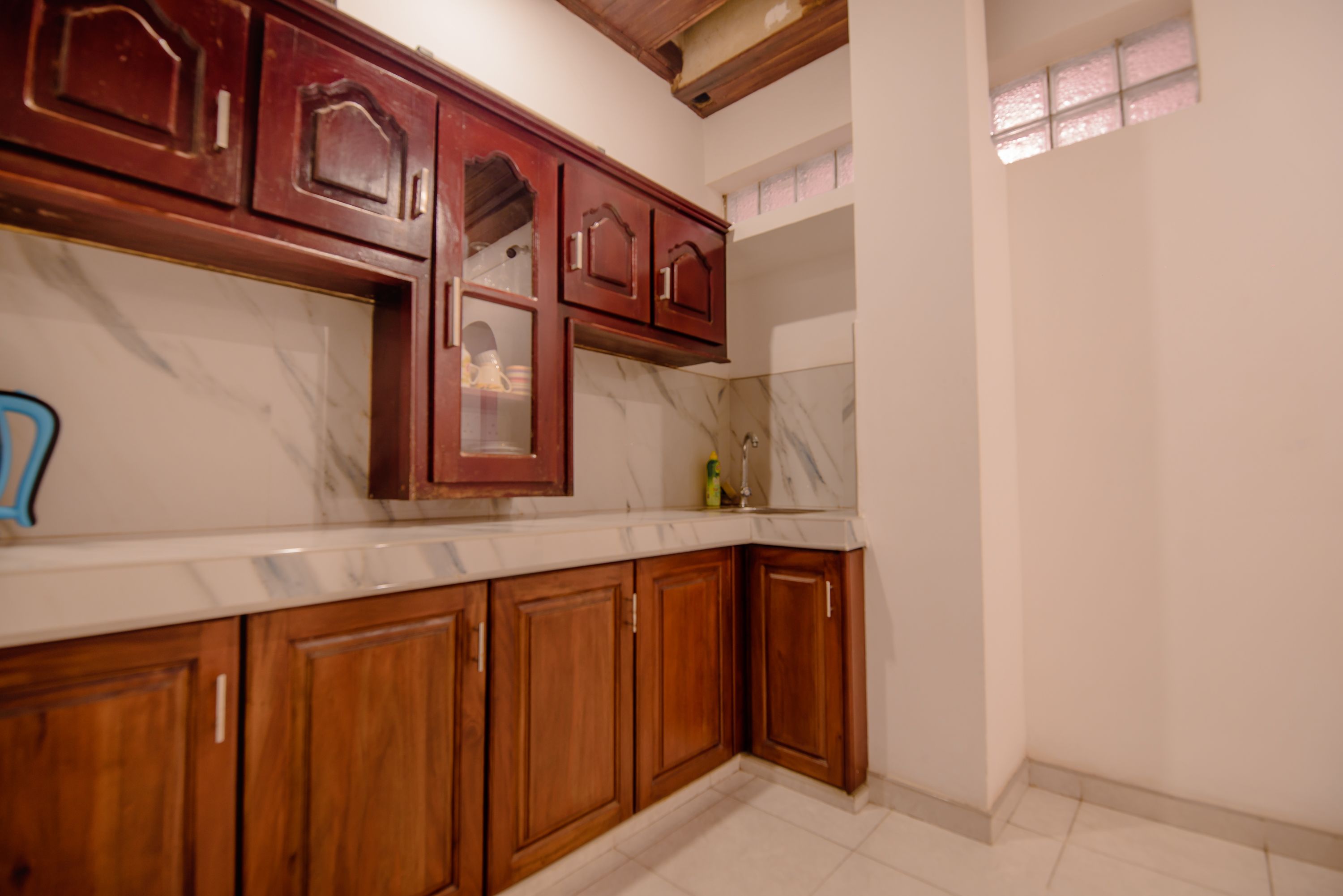 A kitchen with wooden cabinets, a marble countertop, and a window with pink-tinted glass.