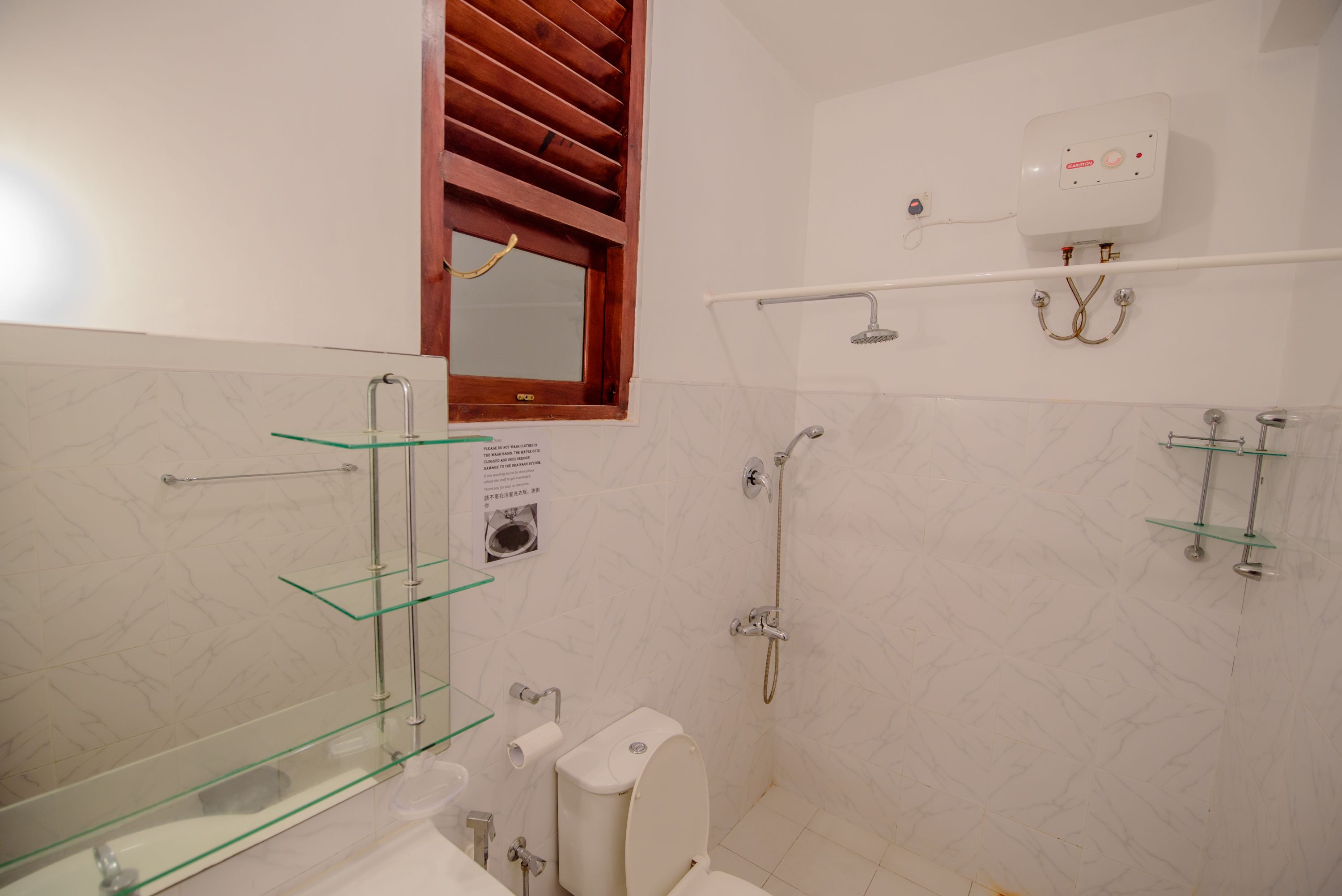 A bathroom with a toilet, a glass shelf, a shower, and a mirror.