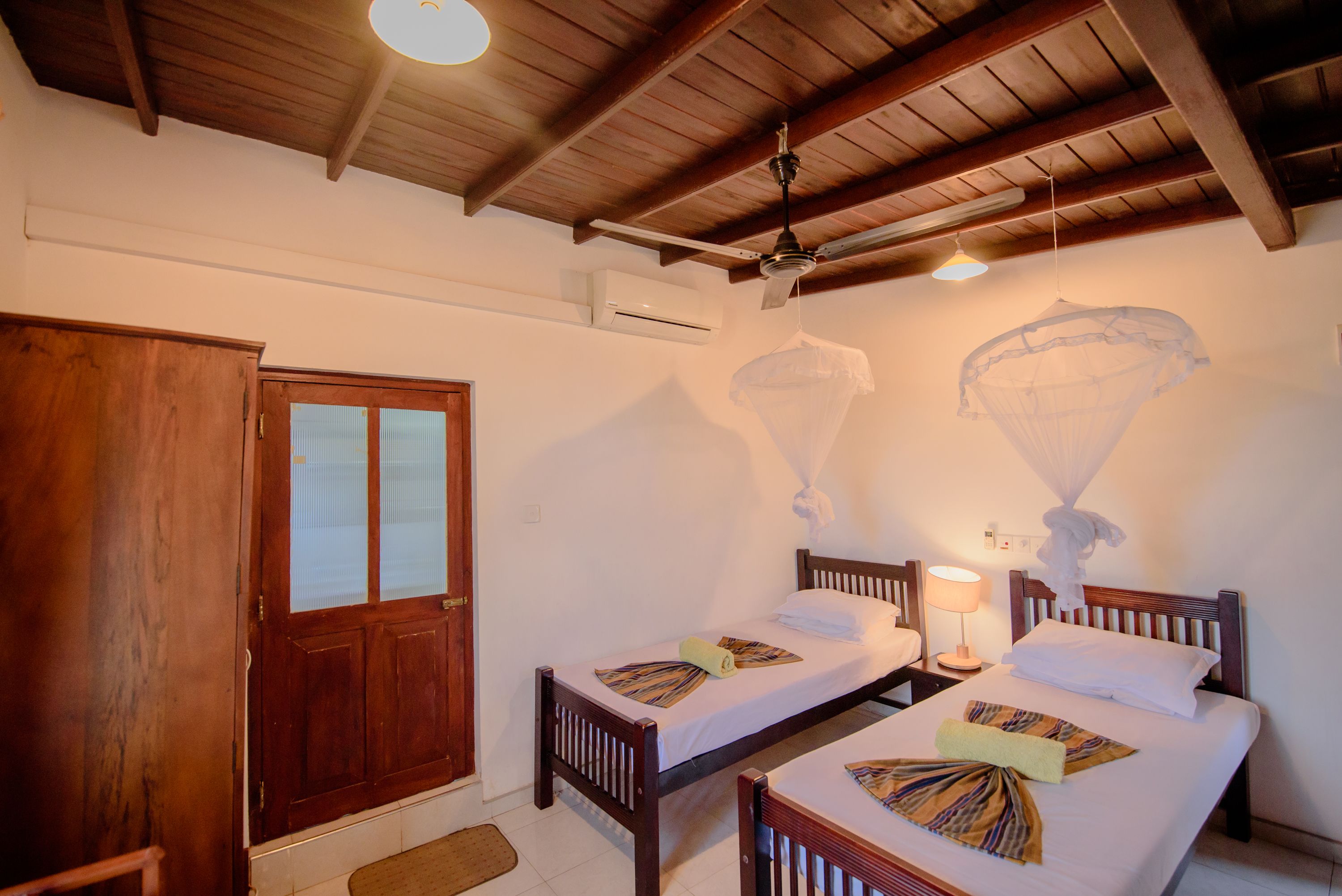 A room with two wooden beds, a wooden wardrobe, a door, and a ceiling fan.