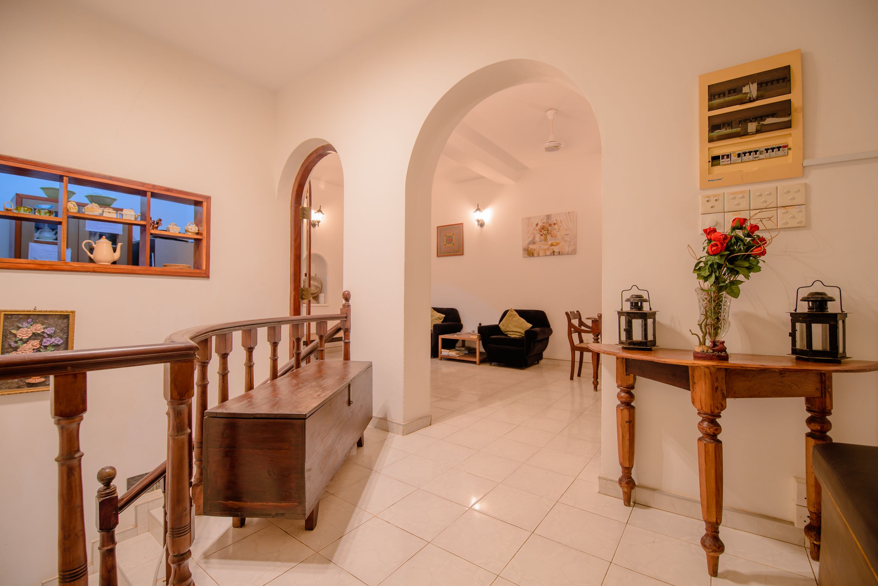 A spacious hallway with a wooden staircase, a seating area with a sofa and chairs, and a table with lanterns and a vase of flowers.