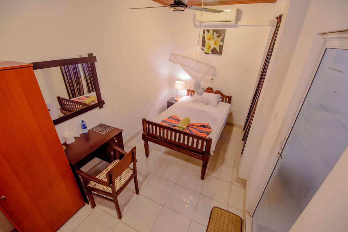 A bedroom with a bed, bedside table, chair, and a desk with a chair.