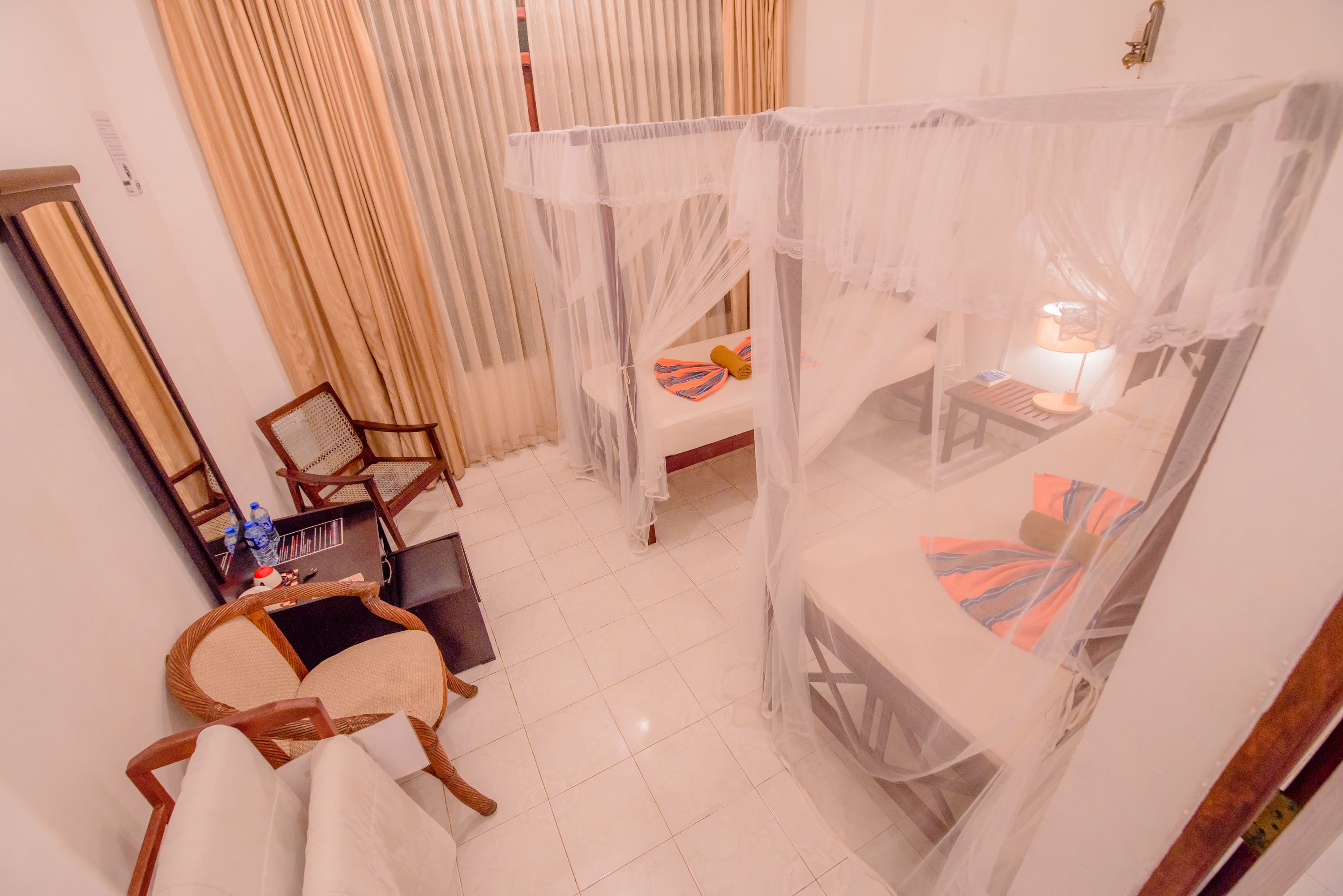 A room with a bed under a canopy, a desk with a chair, and a small table with a lamp.