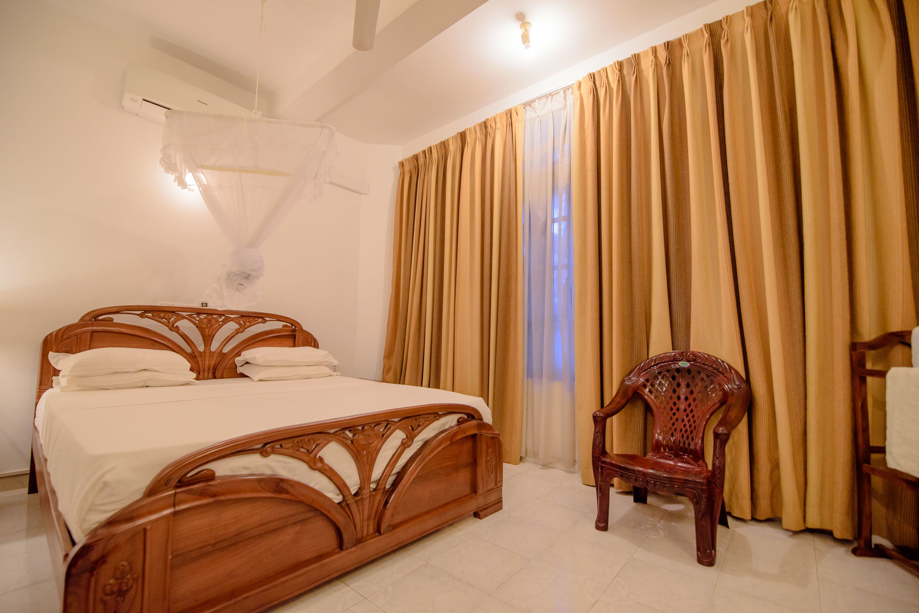 A bedroom with a wooden bed, a wooden chair, and a window with curtains.