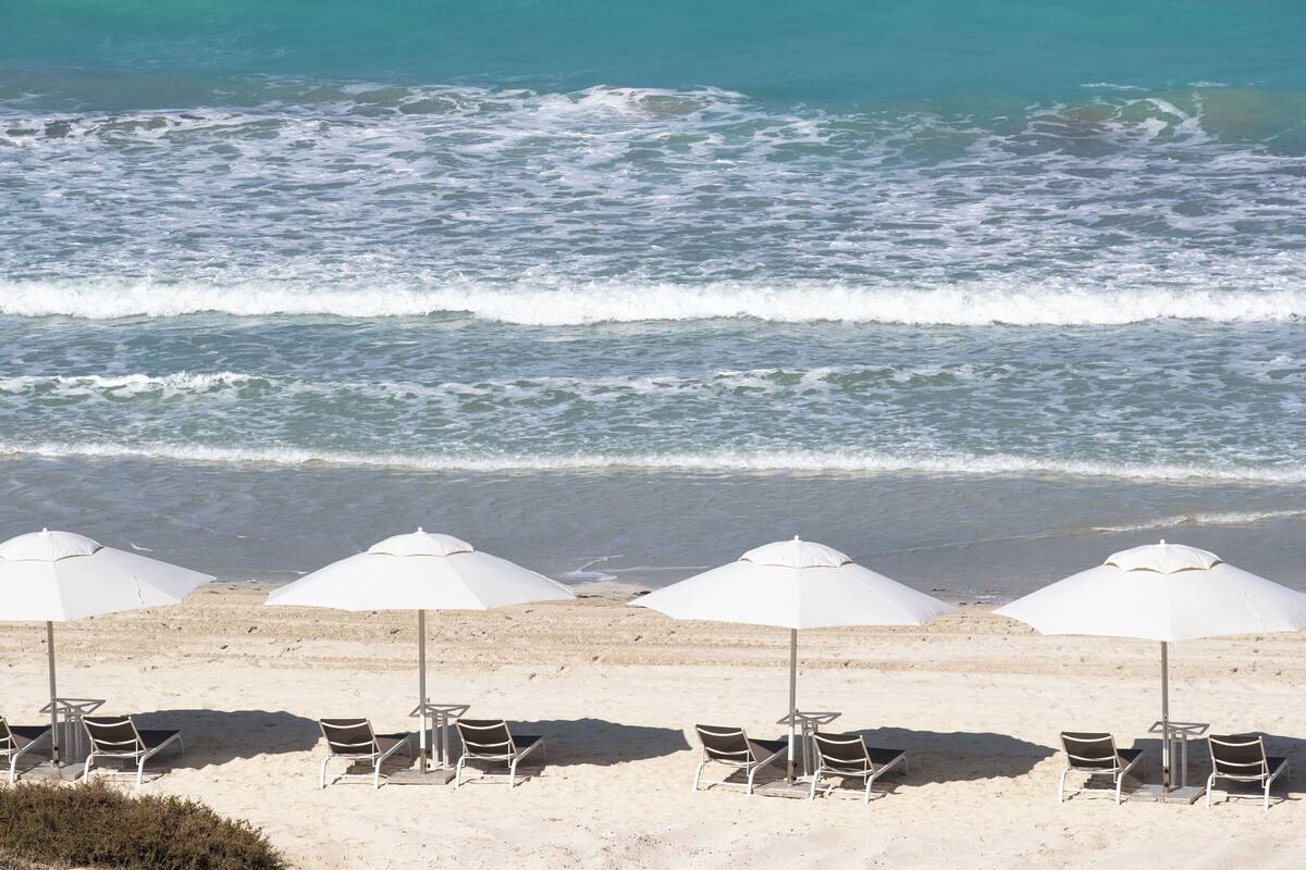 A beach with white umbrellas and chairs, a sandy shore, and waves in the background.