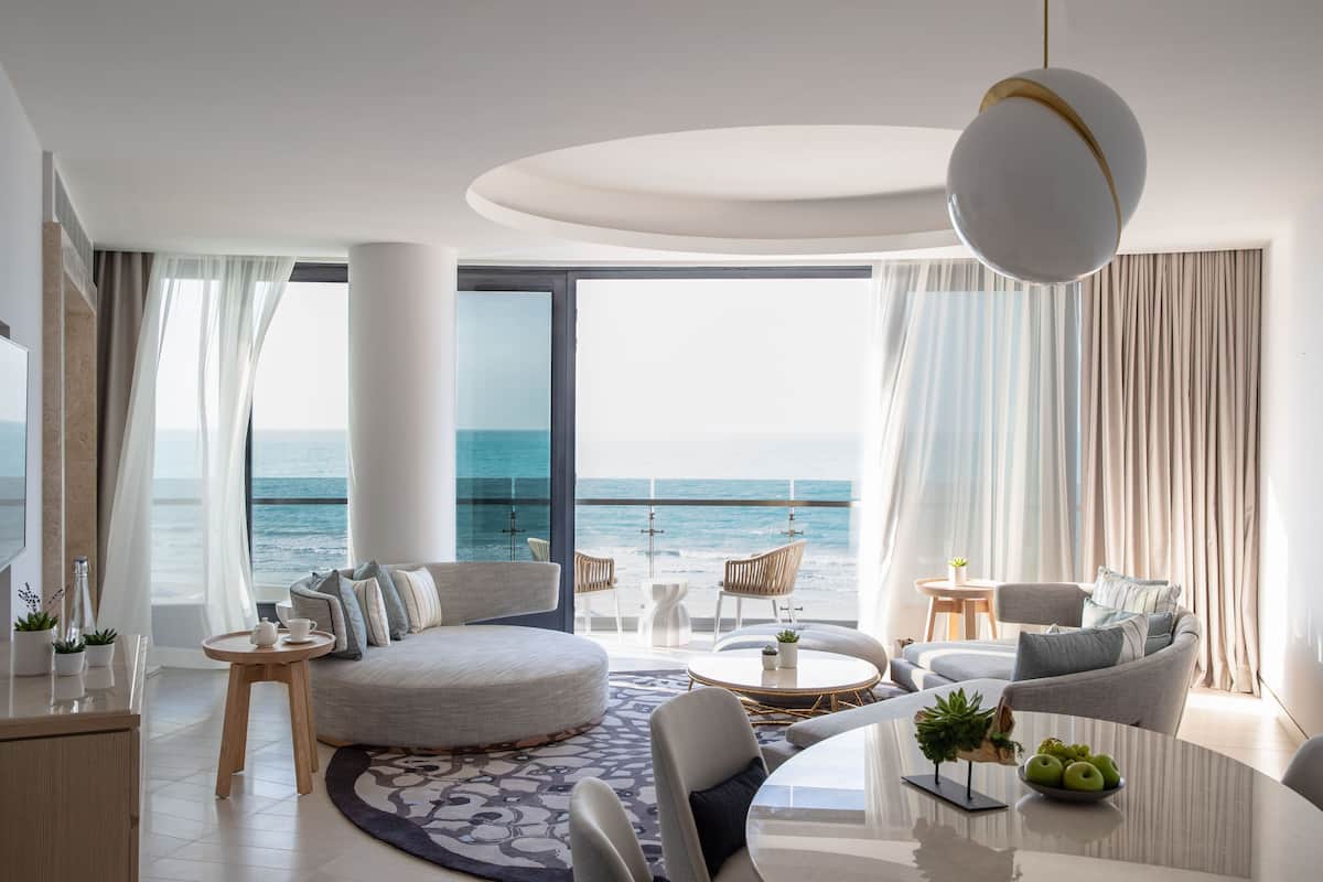 A modern living room with a large sofa, round coffee table, and a view of the ocean.