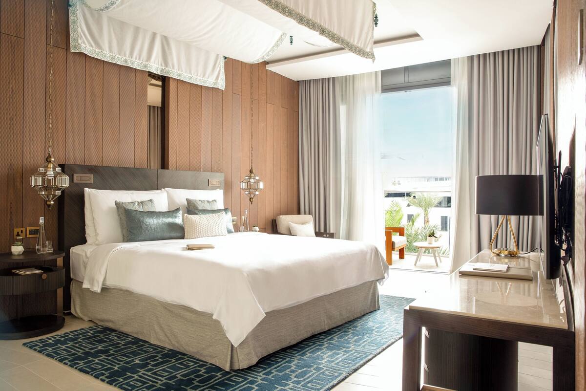 A modern hotel room with a large bed, a desk, and a view of the outdoors.
