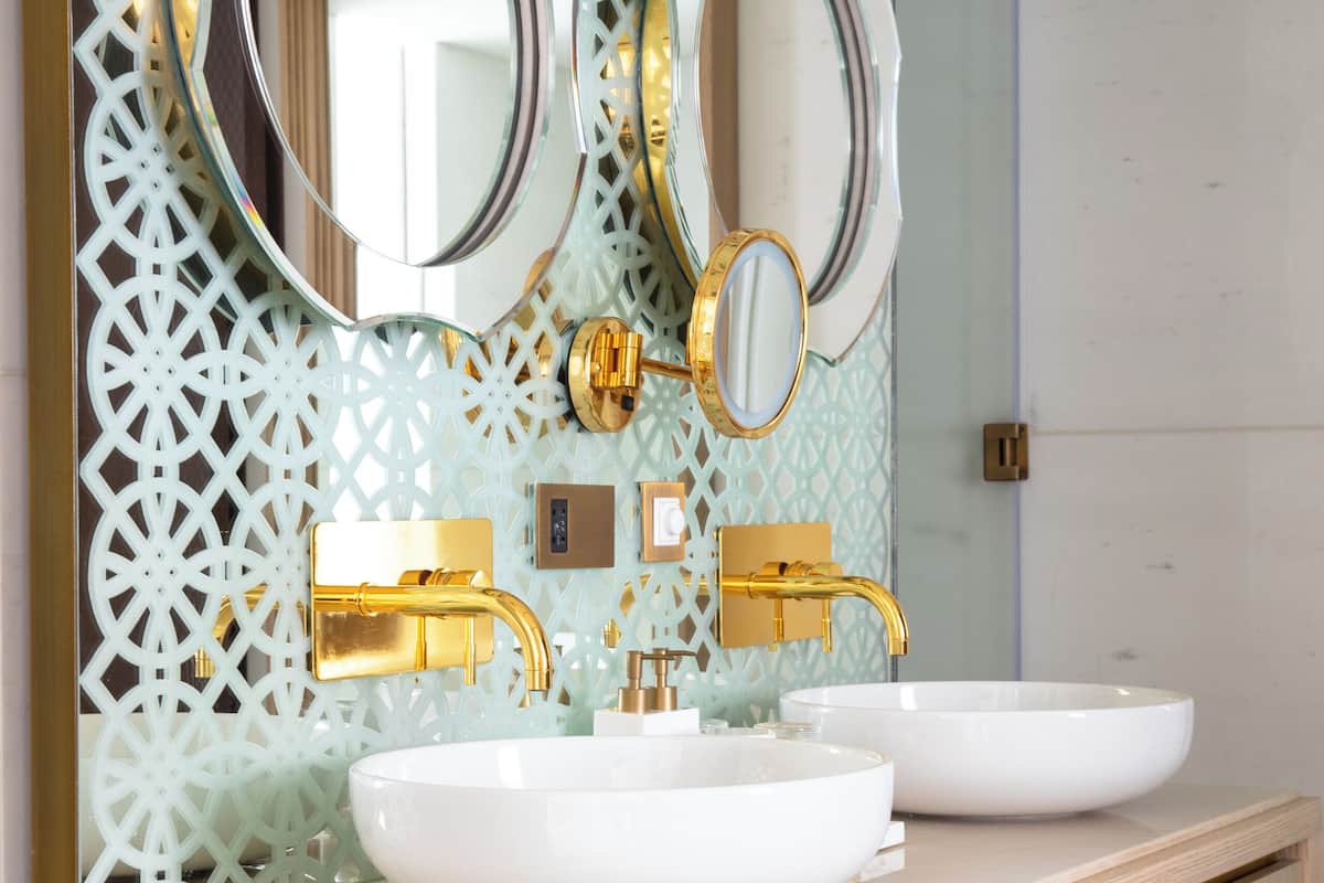 A bathroom with two sinks, gold faucets, and a decorative mirror.
