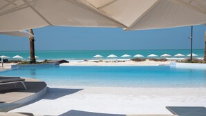 A poolside area with lounge chairs and umbrellas, overlooking a beach with a clear blue ocean. - Jumeirah Saadiyat Island Abu Dhabi (Abu Dhabi)