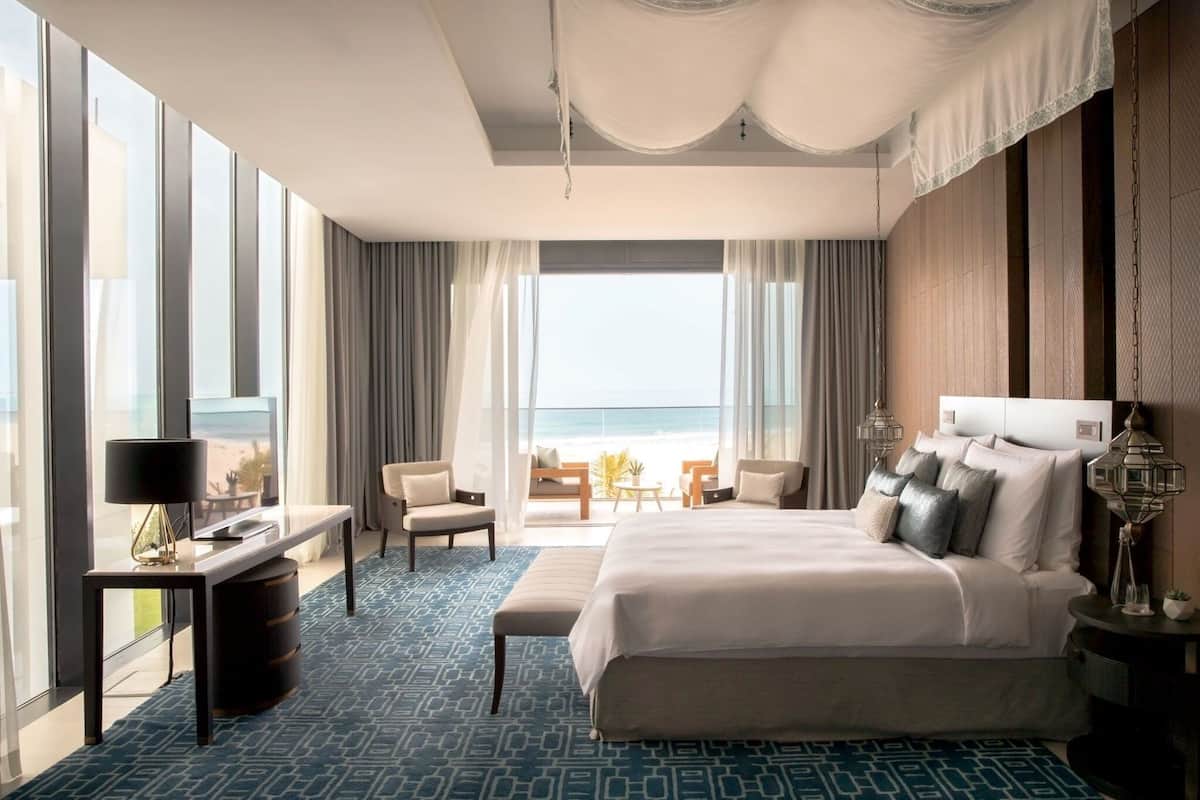 A hotel room with a large bed, a desk, a chair, and a view of the ocean.