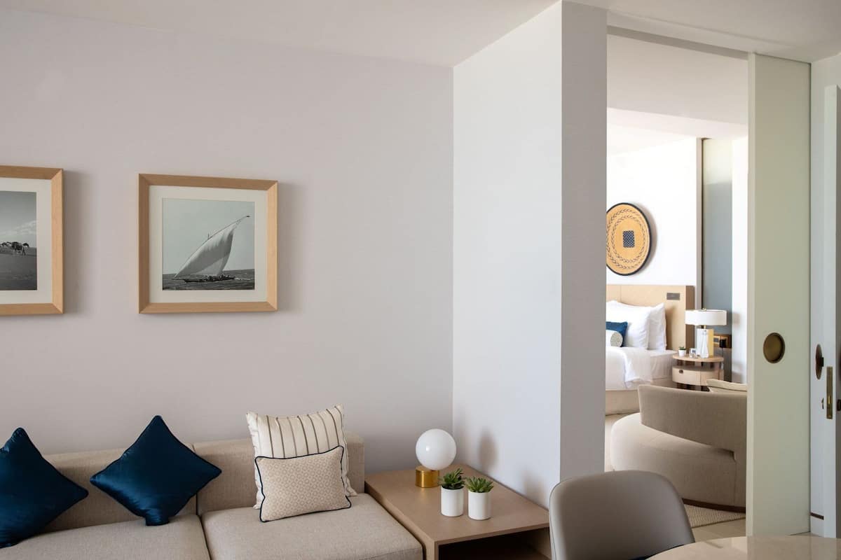 A modern hotel room with a beige sofa, a small side table with a lamp, and two framed pictures on the wall.