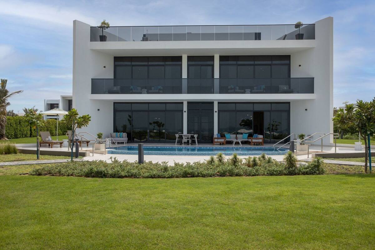 A modern two-story house with a swimming pool, outdoor seating, and a well-maintained lawn.