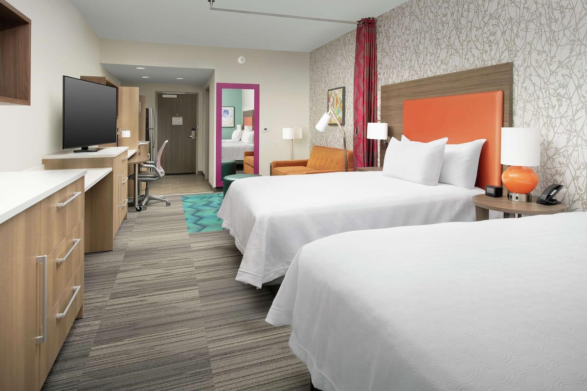 Une chambre d’hôtel avec deux lits, un bureau avec une télévision, une chaise et une petite table avec une lampe.
