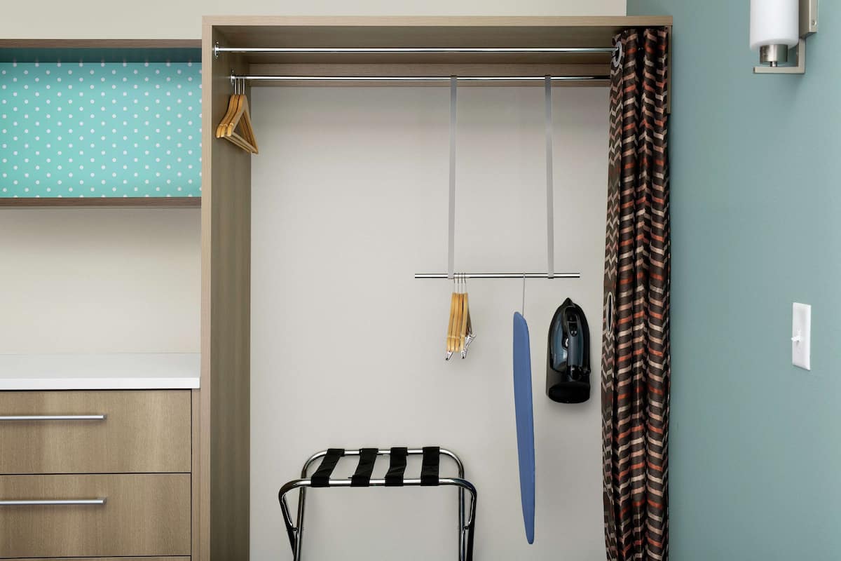 Une chambre avec une armoire en bois, un étendoir métallique, une serviette bleue et un rideau à motifs.
