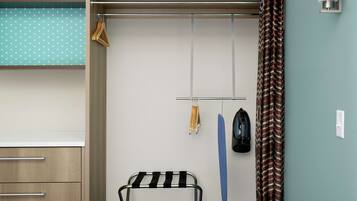 A bedroom with a wooden wardrobe, a metal drying rack, a blue towel, and a patterned curtain.