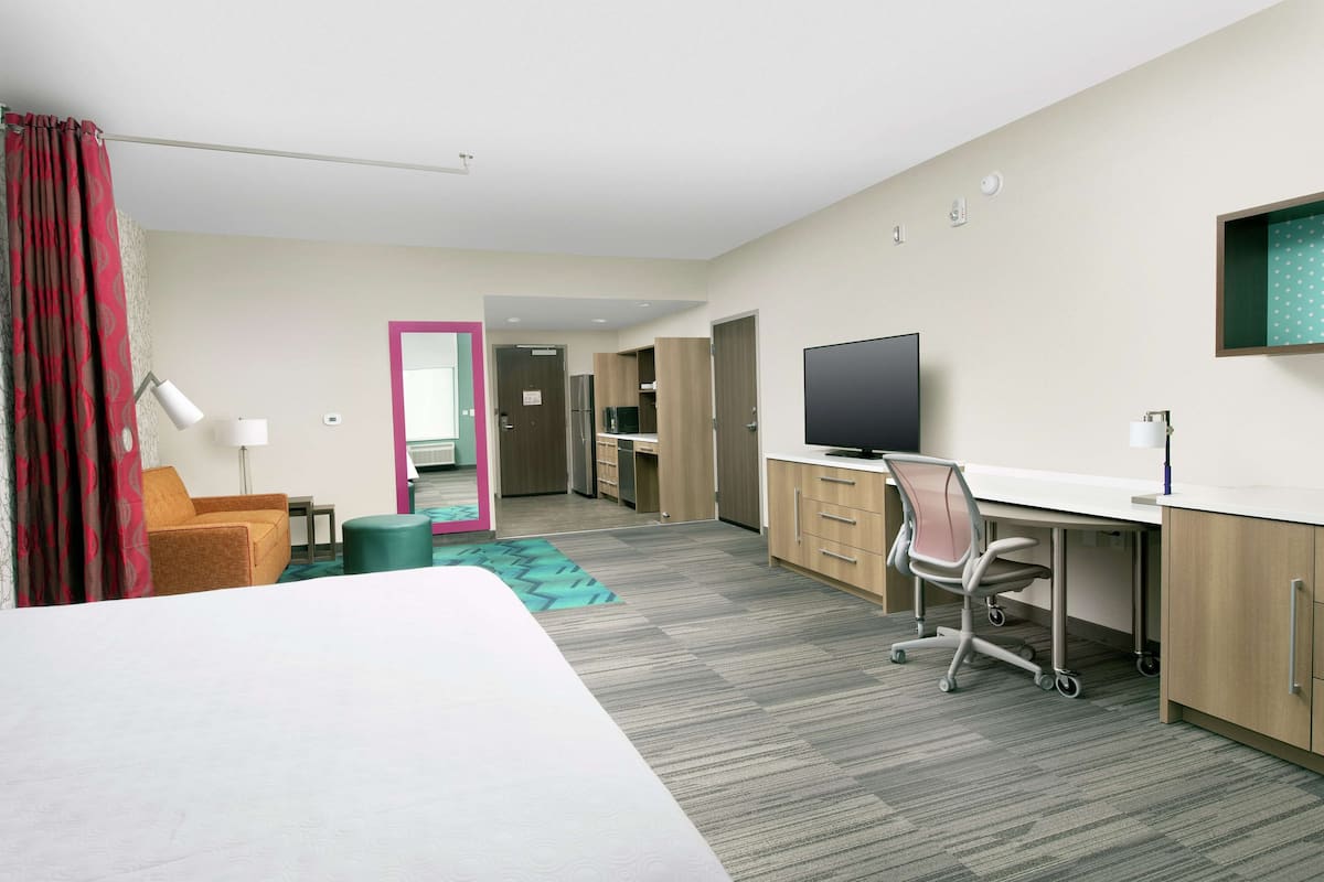 Une chambre d’hôtel avec un lit, un bureau, une chaise, une télévision et une salle de bain visible à travers une porte ouverte.