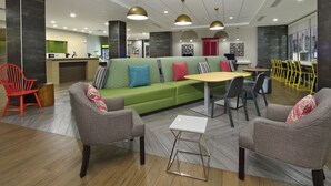 A modern lobby with a green sofa, grey armchairs, a small white table, and yellow chairs. - Home2 Suites by Hilton Port Arthur, TX (Port Arthur)