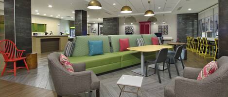 A modern lobby with a green sofa, grey armchairs, a small white table, and yellow chairs.