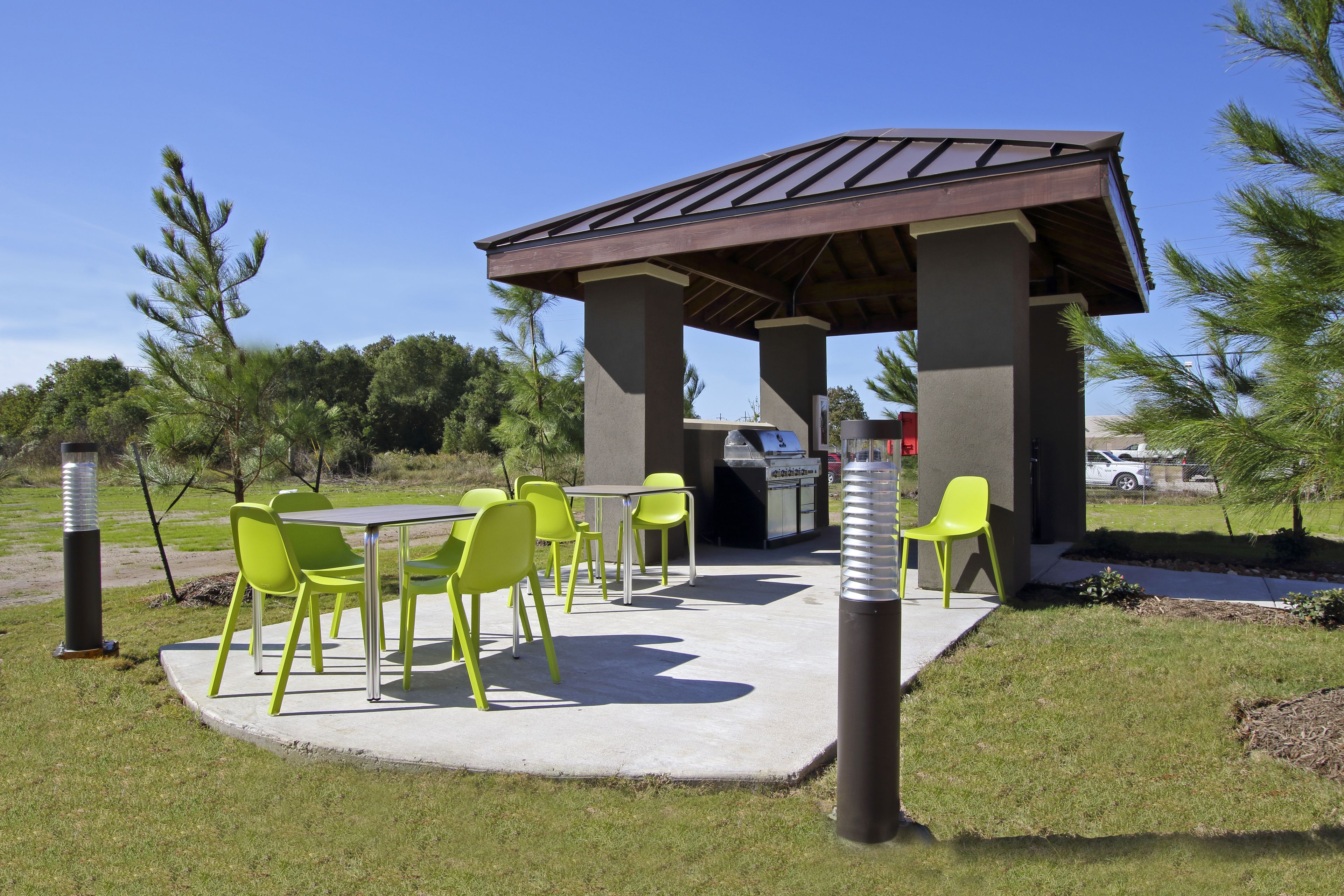 An outdoor patio with a covered grill area, green chairs, and a concrete floor.