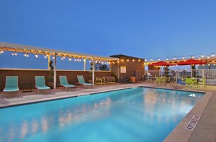 Una piscina con sillas de descanso y sombrillas, rodeada por una zona techada con luces colgantes.