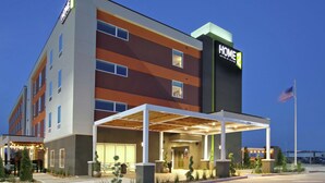 A modern hotel with a covered entrance, outdoor seating, and a sign indicating it is a Home Suites by Hilton. - Home2 Suites by Hilton Port Arthur, TX (Port Arthur)