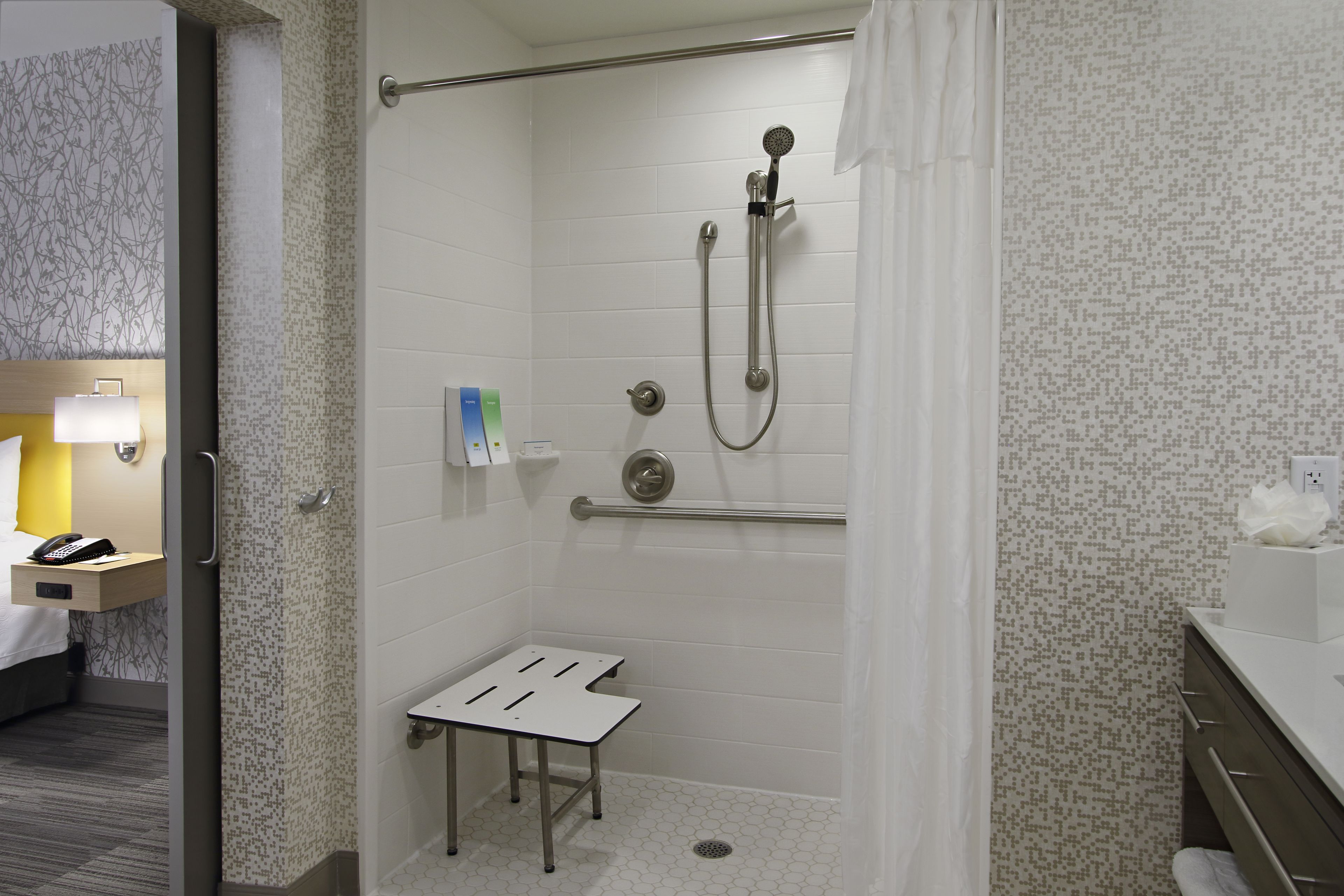 A hotel bathroom with a shower, a small table, and a towel rack.