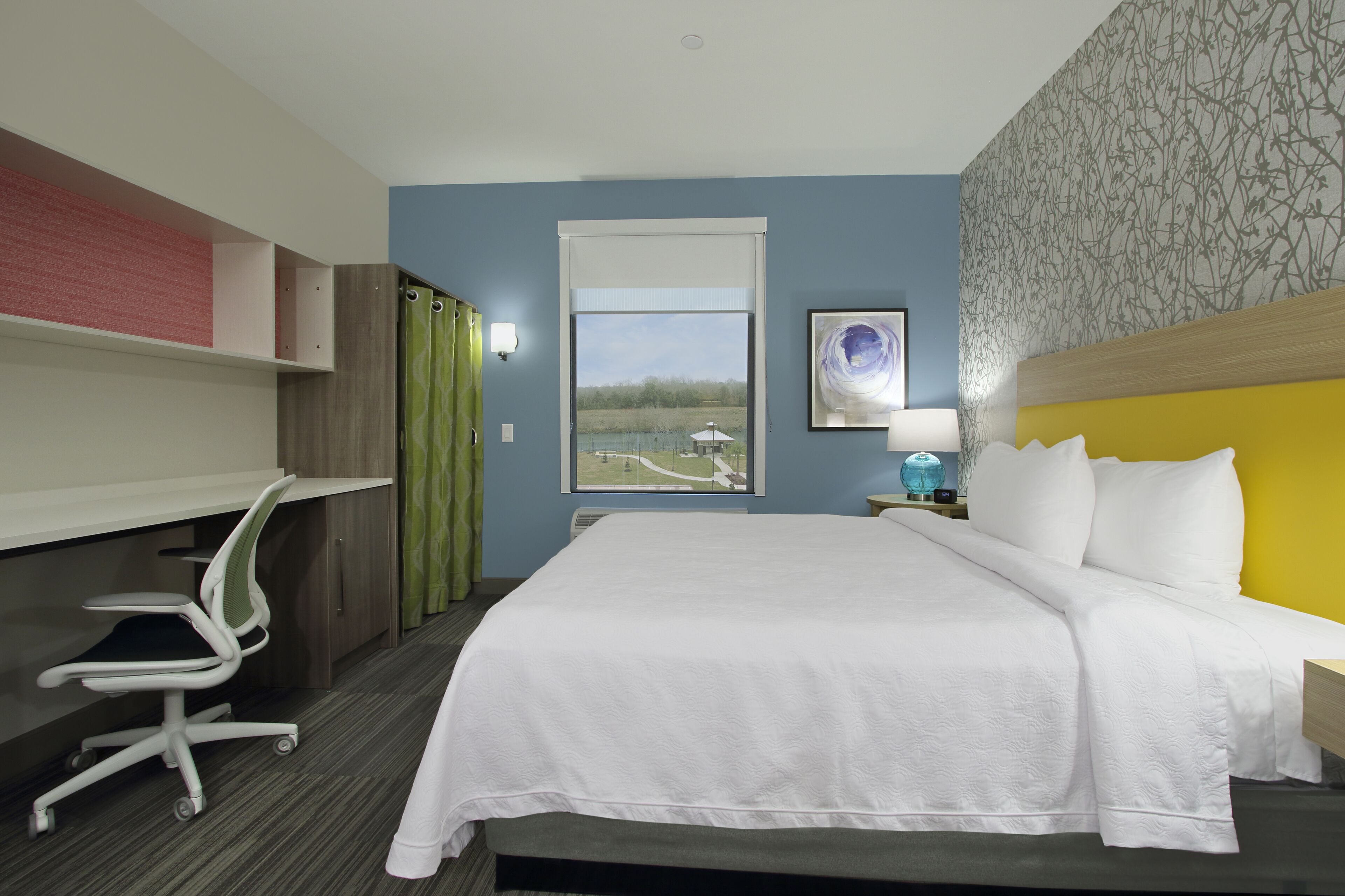 Une chambre d’hôtel comprenant un lit, un bureau et une chaise, une fenêtre avec vue et une table de chevet avec une lampe.
