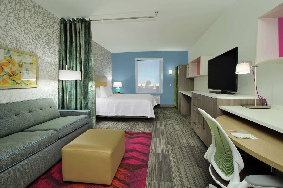Une chambre d’hôtel avec un lit, un canapé, un bureau, une télévision et une fenêtre donnant sur un beau paysage.