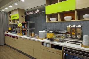 Disposición de buffet con secciones identificadas para recipientes, utensilios y un microondas.
