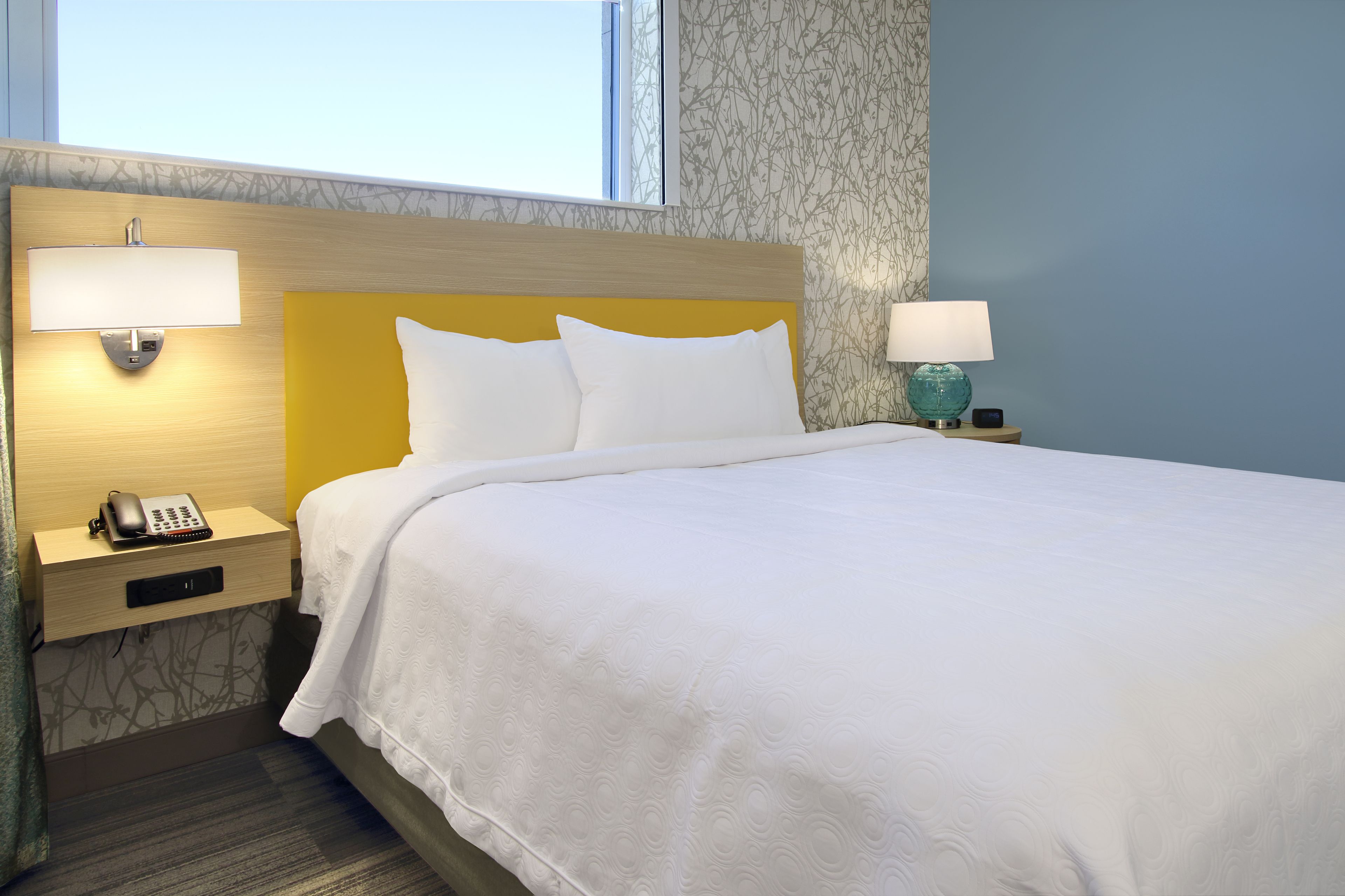 Una habitación de hotel con cama, lámparas de noche, teléfono y ventana.