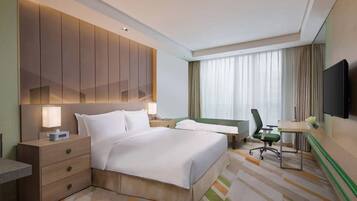 Habitación de hotel con una cama grande, un escritorio, una silla, un televisor y una mesita de noche.