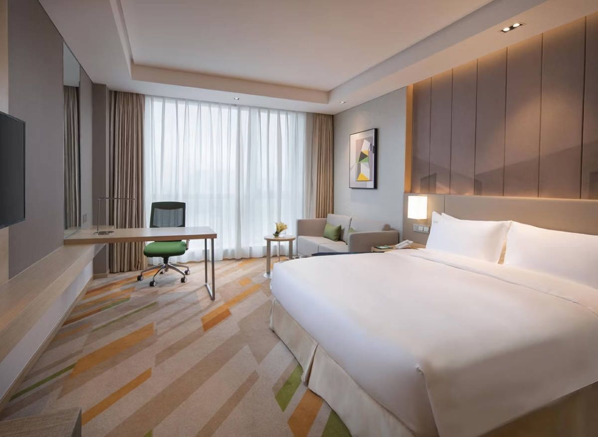 Een hotelkamer met een groot bed, een bureau met stoel, een televisie en een raam met gordijnen.