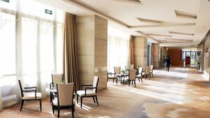 Een ruime hotellobby met een modern design, met een lange gang met zitgedeeltes en een groot raam dat natuurlijk licht binnenlaat.