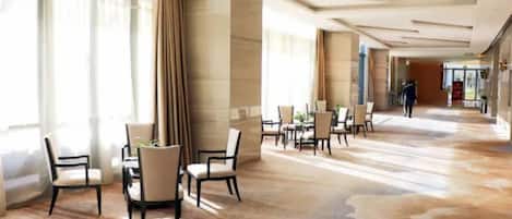 Un espacioso vestíbulo de hotel con un diseño moderno, que presenta un largo pasillo con zonas de estar y un amplio ventanal que proporciona luz natural.