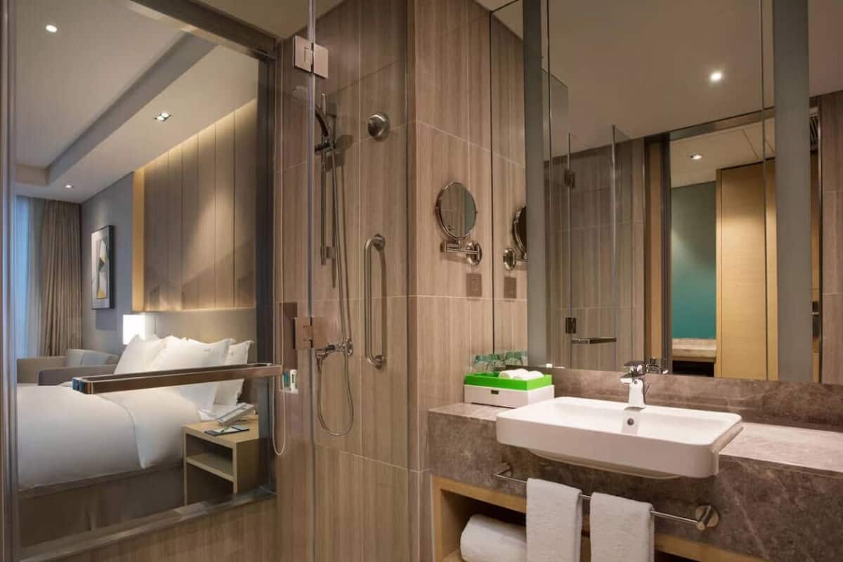Une salle de bain d’hôtel moderne, dotée d’une douche à l’italienne, d’un grand miroir, d’un lavabo et d’un meuble-lavabo avec des serviettes.