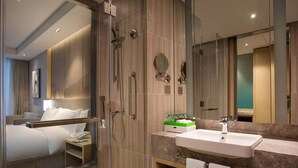 Een moderne hotelbadkamer met een inloopdouche, een grote spiegel, een wastafel en een badkamermeubel met handdoeken.
