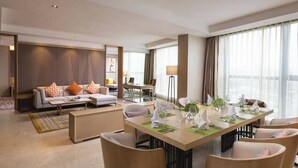 Ein modernes Hotelzimmer mit Essbereich, einer Sofagruppe und einem großen Fenster mit Vorhängen.