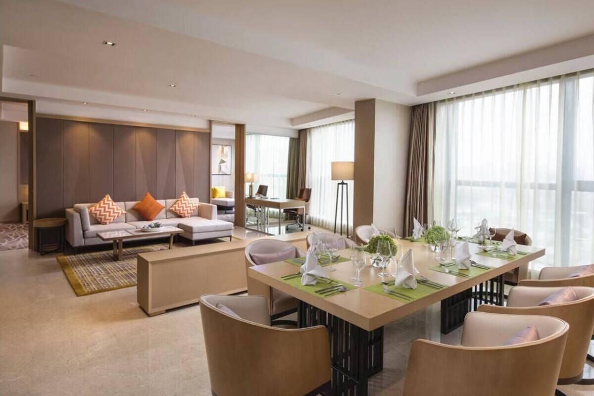 Une chambre d’hôtel moderne dotée d’un coin repas, d’un ensemble de canapés et d’une grande fenêtre avec des rideaux.