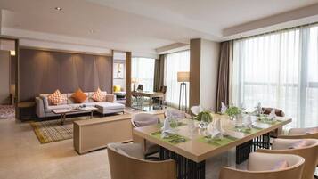 A modern hotel room with a dining area, a sofa set, and a large window with curtains.