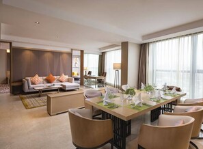 Ein modernes Hotelzimmer mit Essbereich, einer Sofagruppe und einem großen Fenster mit Vorhängen.